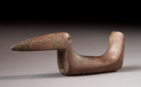 Three-quarter view of a birdstone made of smoothed brown stone with grey marbling that could fit in the hand. There is a long pointed beak, slim body and upright tail.